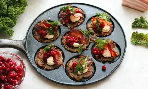 Små, gyllene rårakor i en gjutjärnspanna, toppade med krämig ost, krispigt bacon, lingon och grönkål. Ett läckert råraka recept!