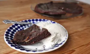 En bit kladdkaka i långpanna serveras med vaniljglass på en blåvit prickig tallrik.