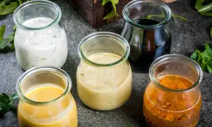Fem glasburkar med olika dressing till sallad: krämig vit, gul, ljusbrun, mörk och en med frön.