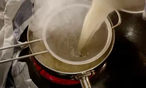Varm buljong silas genom en finmaskig sil ner i en kastrull. Ånga stiger från den varma vätskan.