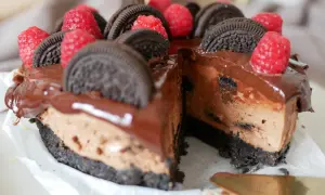 En chokladig oreo cheesecake med hallon och chokladglasyr. En bit är bortskuren.