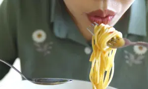En person äter spaghetti med gaffel och sked. Det är en härlig pastarätt.