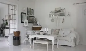 Ett rum med shabby chic inredning. En vit soffa med kuddar, ett vitt bord med ljus och en rund matta.