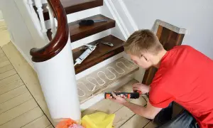 Man renoverar trappa med fogpistol och lim på en trappsteg.