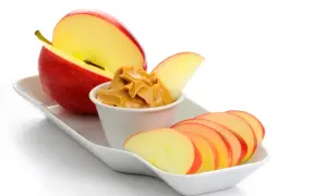 Ett rött äpple, skivat och med en skål jordnötssmör, perfekta kalorisnåla snacks.