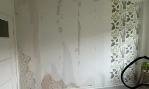 Väggen är delvis avrivet tapet, med fläckar av gammal tapet kvar. En bit med blommig tapet syns till höger.