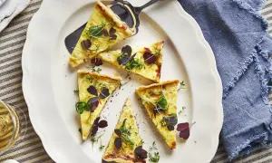 Välskuren quiche lorraine med gyllene skorpa, toppad med färska örter och mörklila blad. Perfekt för en lätt lunch.