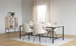 Ett ljust och luftigt rum med matbord och stolar i skandinavisk design. Ett vitrinskåp i trä och glas står till vänster.