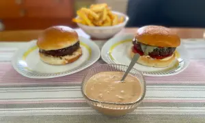 Två saftiga hamburgare med pommes frites och en skål med krämig hamburgerdressing. Perfekt för en mysig hemmakväll!