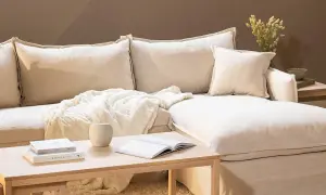En bekväm soffa med pastell inredning, prydd med mjuka kuddar och en fluffig pläd. Ett soffbord i trä med böcker och en vas fulländar den lugna atmosfären.