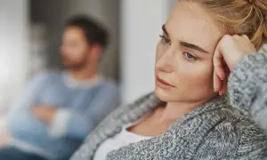 En kvinna med en bekymrad blick vilar huvudet mot handen. I bakgrunden sitter en man med armarna i kors, kanske en symbol för att han är emotionellt omogen.