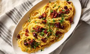 En skål med spaghetti toppad med soltorkade tomater, oliver och persilja. Ett enkelt och gott pasta recept.