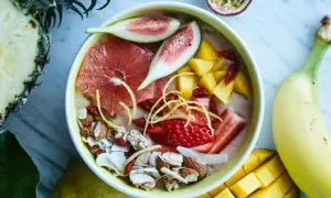 En skål med nyttiga smoothies fylld med jordgubbar, mango, grapefrukt, nötter och kokosflingor. Omgiven av färsk frukt som ananas och banan.
