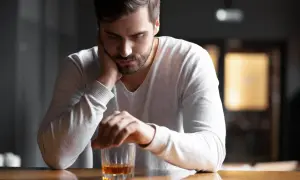 En man sitter ensam vid ett bord med ett glas whisky framför sig. Han ser nedstämd ut, som om min man dricker varje dag och han inte kan sluta.