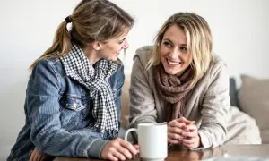 Två kvinnor ler mot varandra över en kaffemugg. De ser ut att vara vänner som pratar, inte alls som otacksamma vuxna barn.