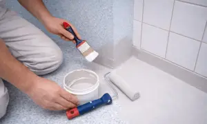Måla våtrumstapet från 70-talet med grå färg. En pensel och en roller ligger bredvid en färgburk.