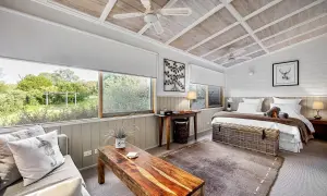 Sovrum i rustik stil med träpanel i taket, bekväm säng och soffa med utsikt över grönskande natur.
