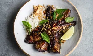 En skål med ris och glaserad, grillad aubergine toppad med jordnötter, chili och mynta. En limeklyfta ligger bredvid.