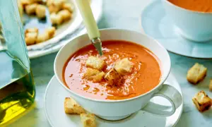 En skål med krämig gazpacho, toppad med krutonger. Bredvid står en karaff med olivolja, perfekt för ditt gazpacho recept.
