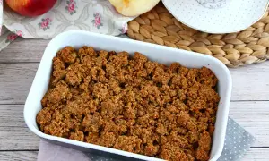 En härlig glutenfri frukost med äppelcrisp i en vit form, äpplen och en kopp te i bakgrunden.