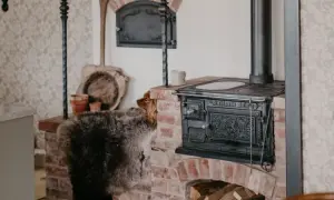 En hund kikar fram bakom en fårskinnspläd vid en gammal gjutjärnskamin. Perfekt lantlig inredning inspiration med tegel och rustika detaljer.