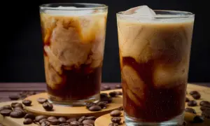 Två glas med krämigt iskaffe, perfekt för ett enkelt iskaffe recept. Kaffebönor sprider sig runt glasen.