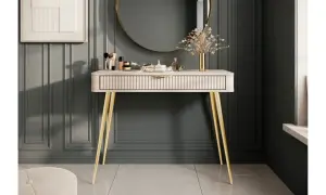Ett elegant sminkbord med guldfärgade ben och en räfflad lådfront. Inspiration för ett stilfullt sminkbord med smink, parfym och en vas med blommor.