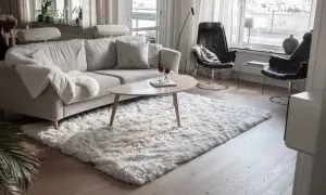 En fluffig, vit matta ligger framför en ljusgrå soffa och skapar en mysig känsla i vardagsrummet.
