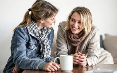 Två kvinnor ler mot varandra över en kaffemugg. De ser ut att vara vänner som pratar, inte alls som otacksamma vuxna barn.