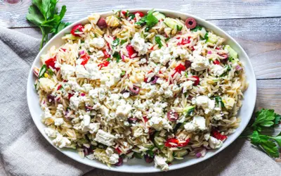 En stor skål med orzo pastasallad, toppad med fetaost, oliver, gurka och paprika. Ett perfekt pastasallad recept för sommaren.
