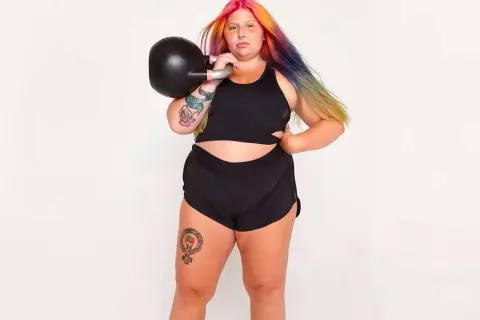 Kvinna med färgglatt hår tränar med kettlebell. Frågan "hur får man smalare lår" kan besvaras med styrketräning som denna.
