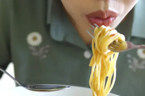 En person äter spaghetti med gaffel och sked. Det är en härlig pastarätt.