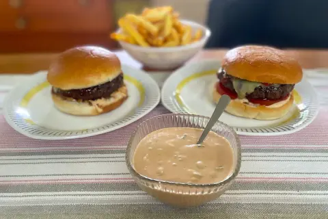 Två saftiga hamburgare med pommes frites och en skål med krämig hamburgerdressing. Perfekt för en mysig hemmakväll!
