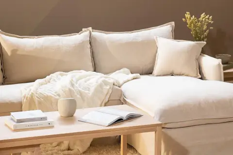 En bekväm soffa med pastell inredning, prydd med mjuka kuddar och en fluffig pläd. Ett soffbord i trä med böcker och en vas fulländar den lugna atmosfären.