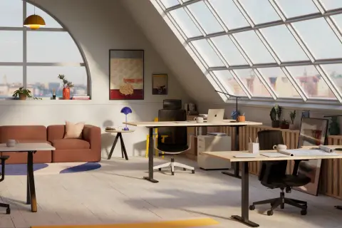 Ett ljust och modernt kontor med flera skrivbord mitt i rummet, soffa och stora fönster med utsikt över en stad.