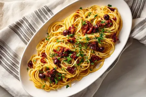En skål med spaghetti toppad med soltorkade tomater, oliver och persilja. Ett enkelt och gott pasta recept.