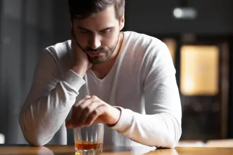 En man sitter ensam vid ett bord med ett glas whisky framför sig. Han ser nedstämd ut, som om min man dricker varje dag och han inte kan sluta.