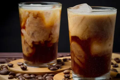 Två glas med krämigt iskaffe, perfekt för ett enkelt iskaffe recept. Kaffebönor sprider sig runt glasen.