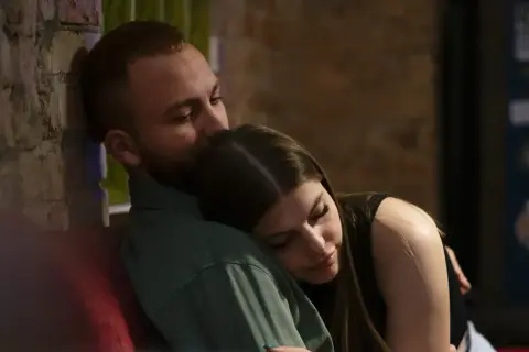 En man kysser en kvinna på pannan. De sitter nära varandra, en bild av trygghet och kärlek, som visar grundstenar i en relation.