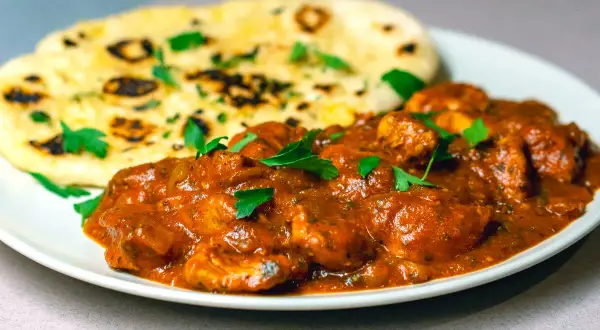 En krämig chicken tikka masala med naanbröd, garnerad med färsk persilja.