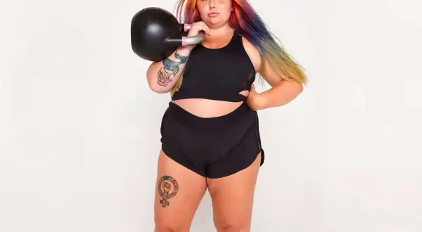 Kvinna med färgglatt hår tränar med kettlebell. Frågan "hur får man smalare lår" kan besvaras med styrketräning som denna.