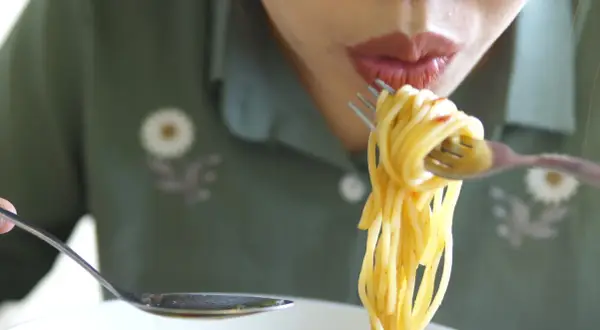En person äter spaghetti med gaffel och sked. Det är en härlig pastarätt.