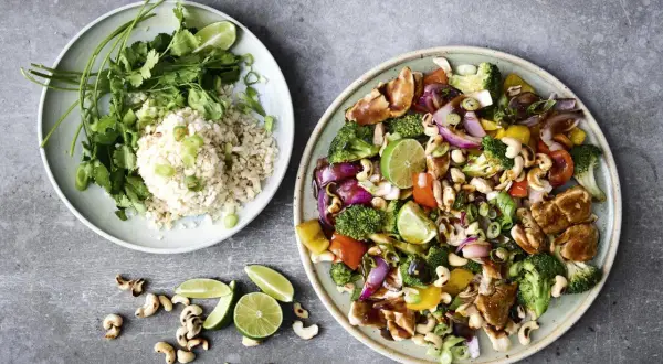 Två tallrikar med nyttig mat: en med ris, koriander och lime, den andra med kyckling, grönsaker och cashewnötter.