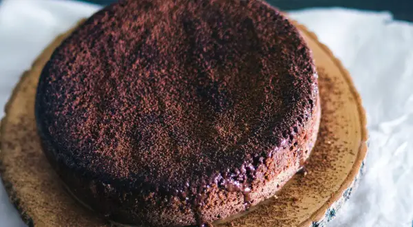 En gudomlig glutenfri chokladkaka, pudrad med kakao, serverad på en träskiva.