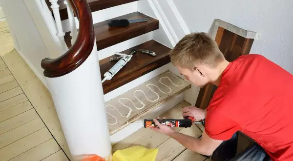 Man renoverar trappa med fogpistol och lim på en trappsteg.