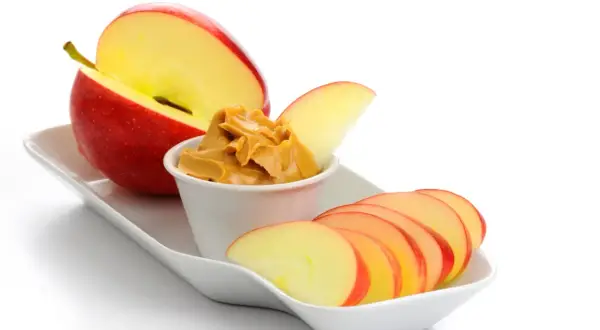 Ett rött äpple, skivat och med en skål jordnötssmör, perfekta kalorisnåla snacks.