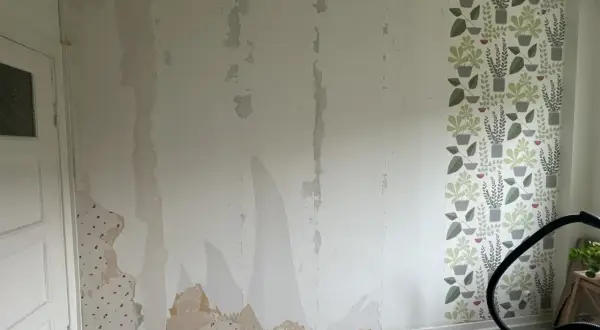 Väggen är delvis avrivet tapet, med fläckar av gammal tapet kvar. En bit med blommig tapet syns till höger.