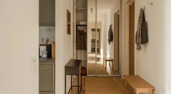 En ljus och inreda hall med en spegelgarderob, en smal konsol, en träbänk och en matta.