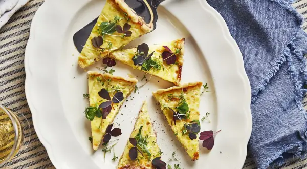 Välskuren quiche lorraine med gyllene skorpa, toppad med färska örter och mörklila blad. Perfekt för en lätt lunch.
