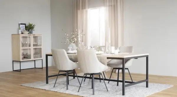 Ett ljust och luftigt rum med matbord och stolar i skandinavisk design. Ett vitrinskåp i trä och glas står till vänster.